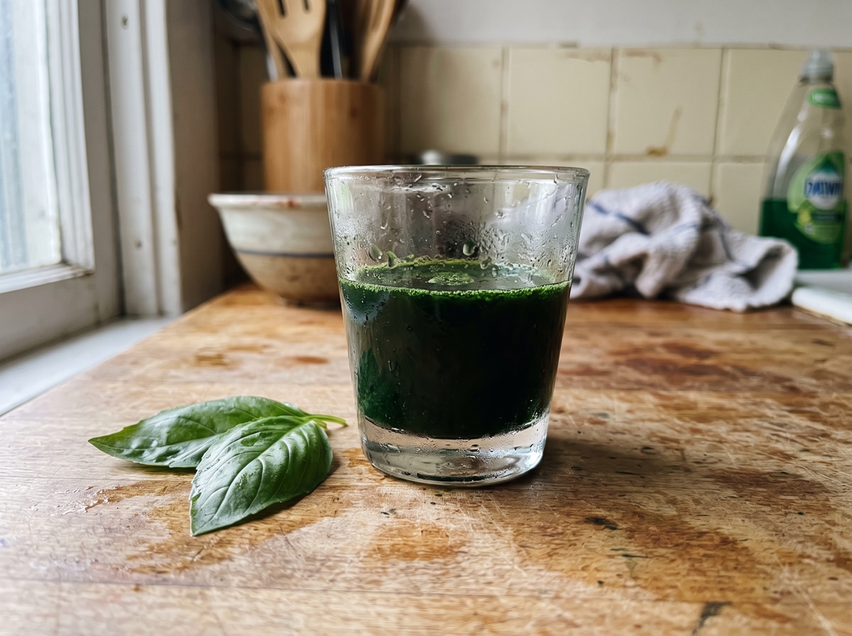 A glass of deep green chlorophyll liquid with fresh leaves